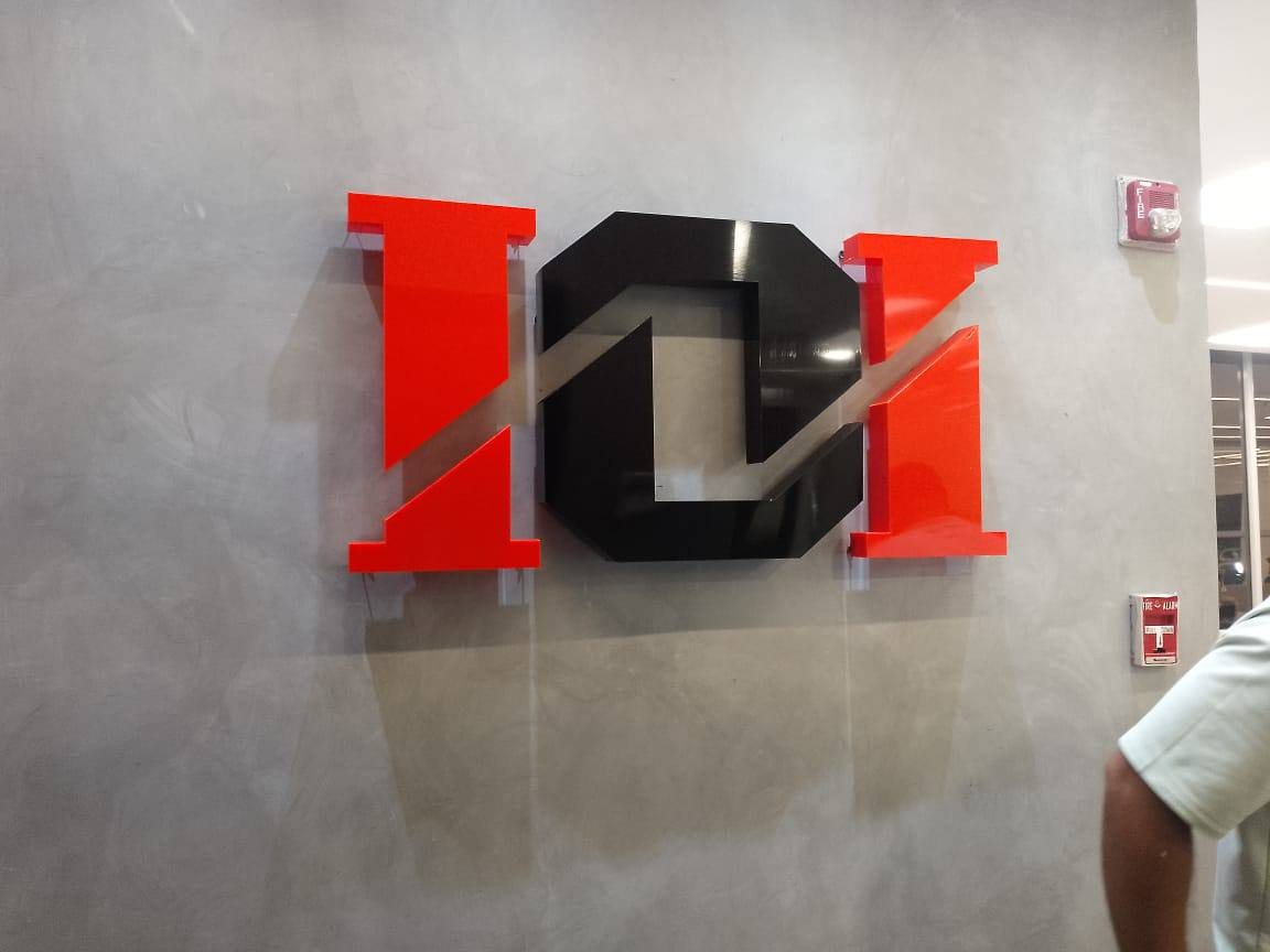 Logo corpóreo en acrílico rojo y negro sobre muro de cemento