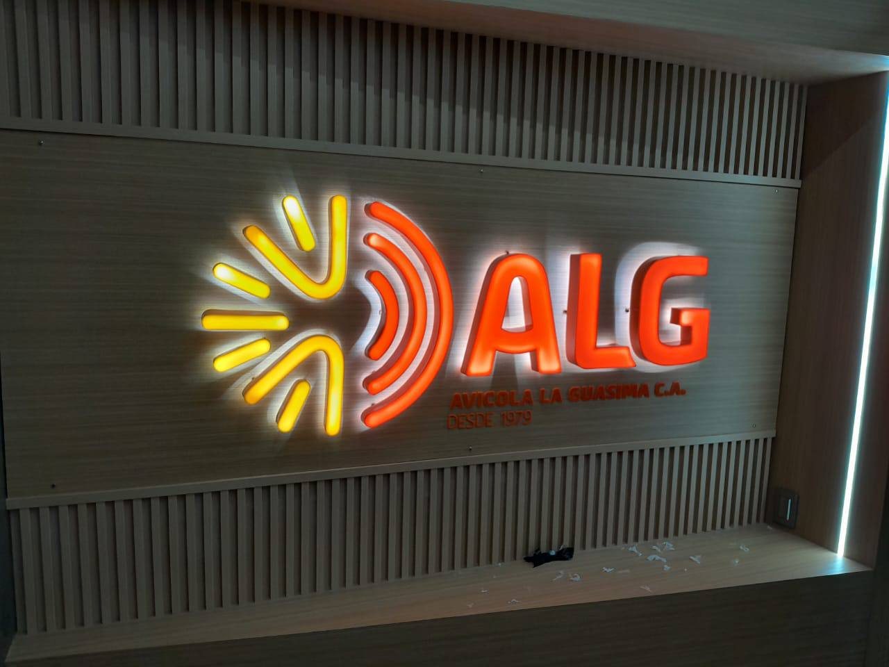 Logo retroiluminado de Avícola La Guásima sobre panel de madera