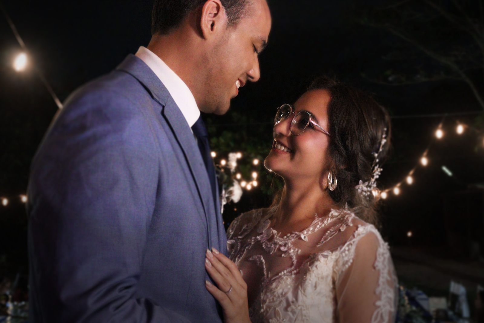 Pareja de novios mirándose bajo luces de guirnalda